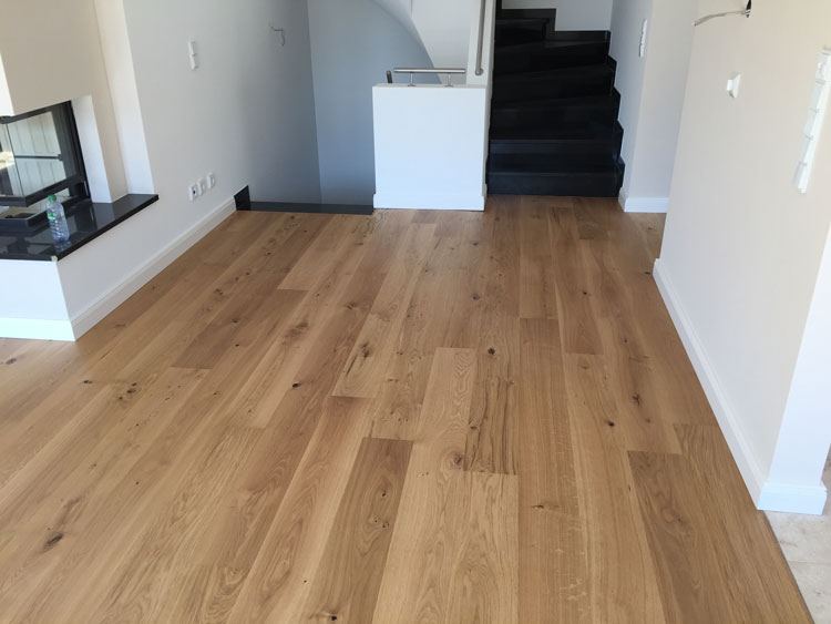 Wohnraum mit verlegtem Eichenparkett, Kamin und dunkler Treppe im Hintergrund
