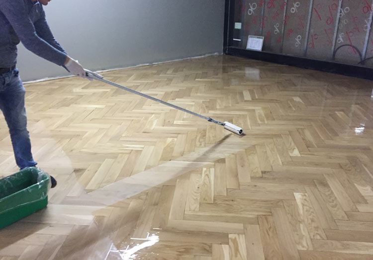 Ein Handwerker trägt mit einer Rolle Öl auf geschliffenes Fischgrätparkett auf