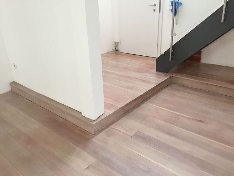 Fertig geschliffener und versiegelter Parkettboden mit Stufe unter einer Treppe