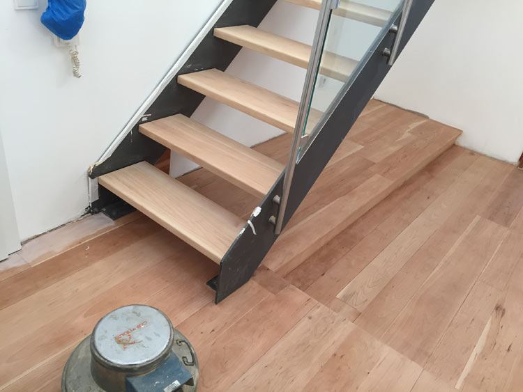 Offene Treppe mit hellen Holzstufen, ein Schleifgerät steht im Vordergrund