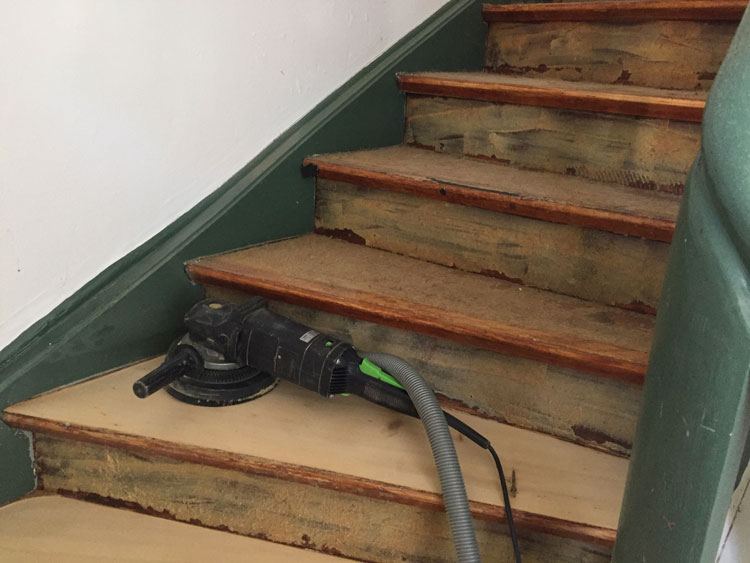 Holzstufen einer gewendelten Treppe werden mit einem Schleifgerät bearbeitet