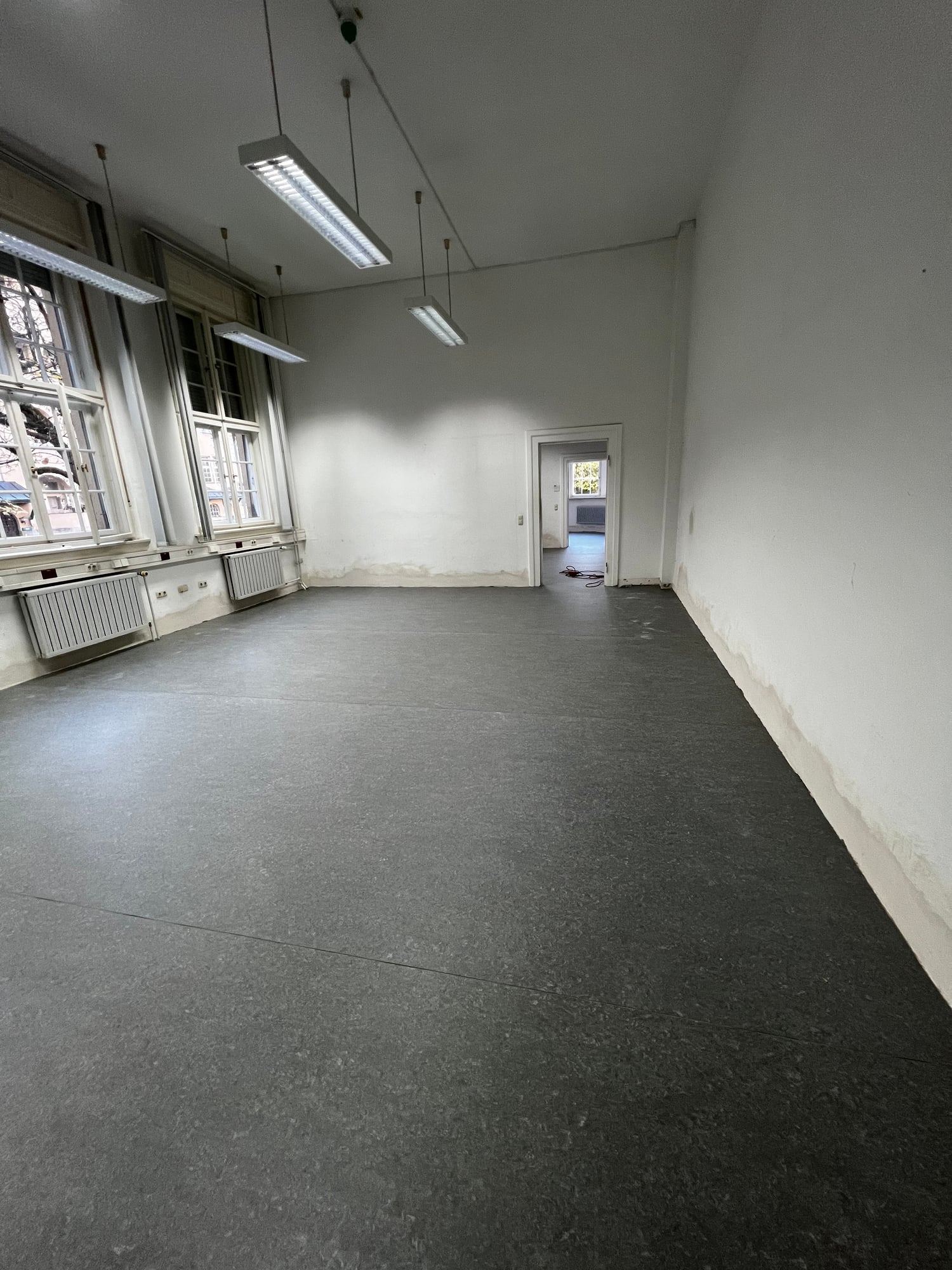 Grauer Linoleumboden in einem langen Büroraum mit Fensterreihe