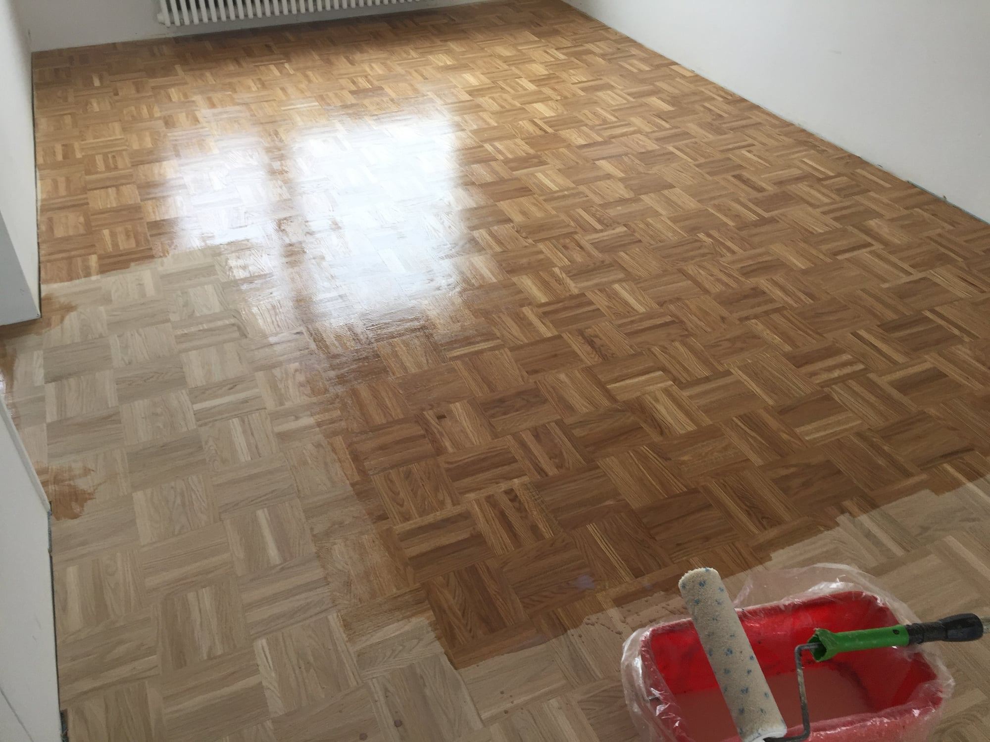 Mosaikparkett wird mit der Rolle versiegelt, ein Teil ist bereits behandelt