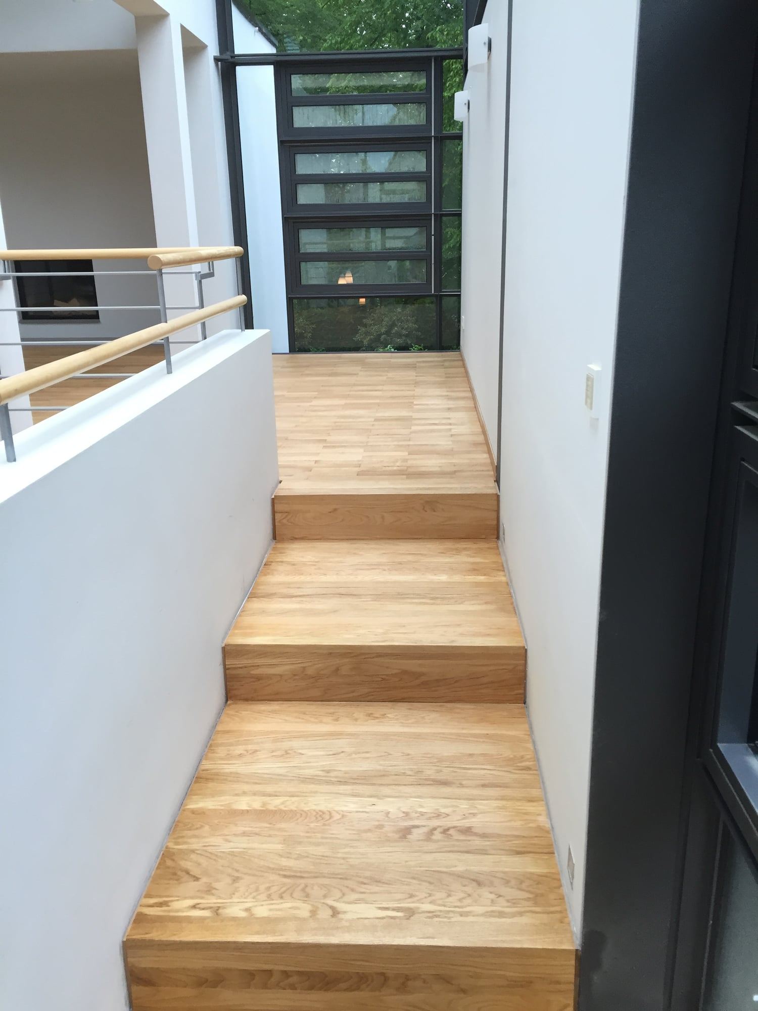 Treppe mit Stufen aus Eiche zwischen weißen Wänden, oben ein Geländer