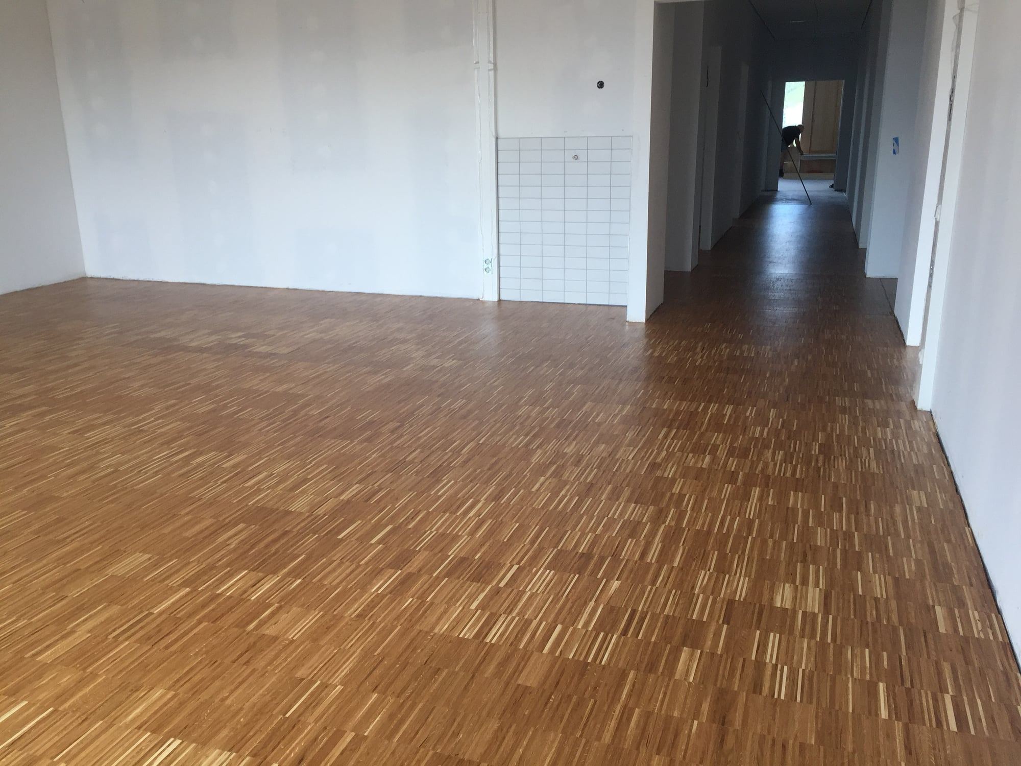 Großer Raum mit fertig verlegtem Industrieparkett, im Hintergrund ein langer Flur